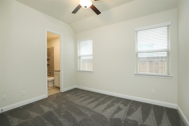 empty room featuring vaulted ceiling, plenty of natural light, and dark colored carpet