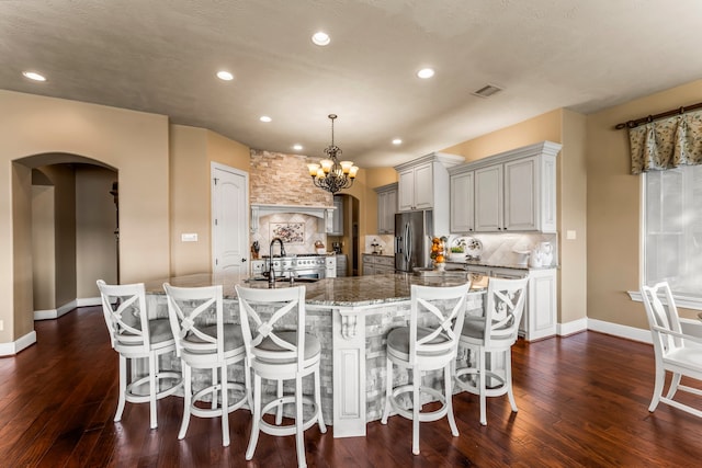 kitchen with sink, stone countertops, stainless steel fridge, decorative light fixtures, and dark wood-type flooring