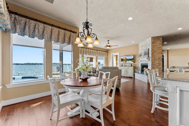 dining room with a fireplace, ceiling fan with notable chandelier, a textured ceiling, dark hardwood / wood-style flooring, and a water view