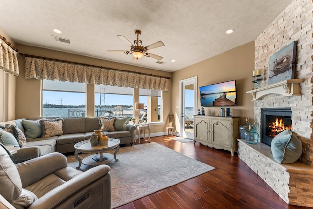 living room featuring ceiling fan, dark hardwood / wood-style flooring, a textured ceiling, a fireplace, and a water view