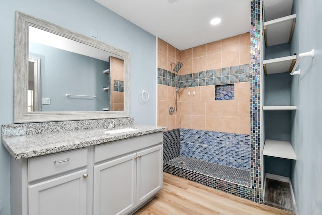 bathroom with hardwood / wood-style flooring, vanity, and tiled shower