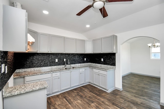 kitchen featuring lofted ceiling, dark wood-type flooring, ceiling fan with notable chandelier, sink, and light stone countertops