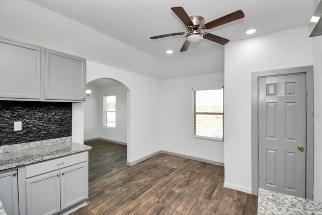 kitchen featuring dark hardwood / wood-style flooring, backsplash, light stone counters, ceiling fan, and gray cabinets