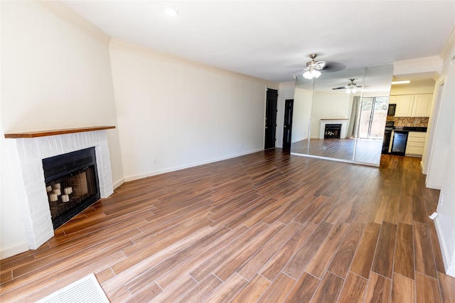 unfurnished living room with hardwood / wood-style flooring, ceiling fan, crown molding, and a brick fireplace