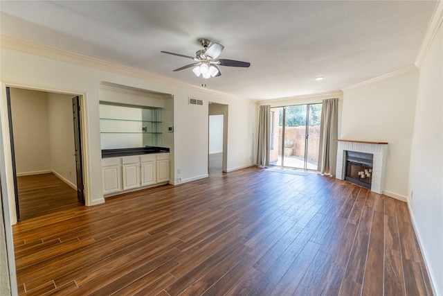 unfurnished living room with dark hardwood / wood-style floors, ceiling fan, ornamental molding, and a brick fireplace