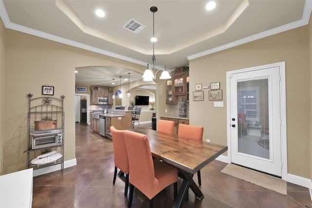 tiled dining room featuring ornamental molding, a tray ceiling, and a chandelier