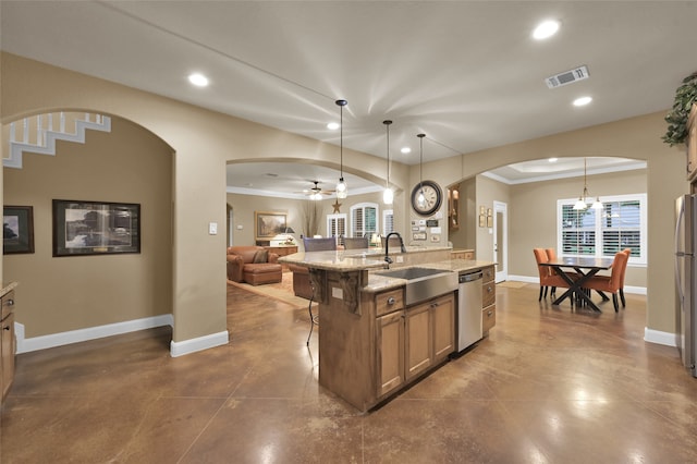 kitchen with sink, stainless steel appliances, decorative light fixtures, ornamental molding, and a kitchen island with sink