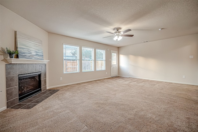 unfurnished living room featuring a tiled fireplace, ceiling fan, a textured ceiling, and dark colored carpet