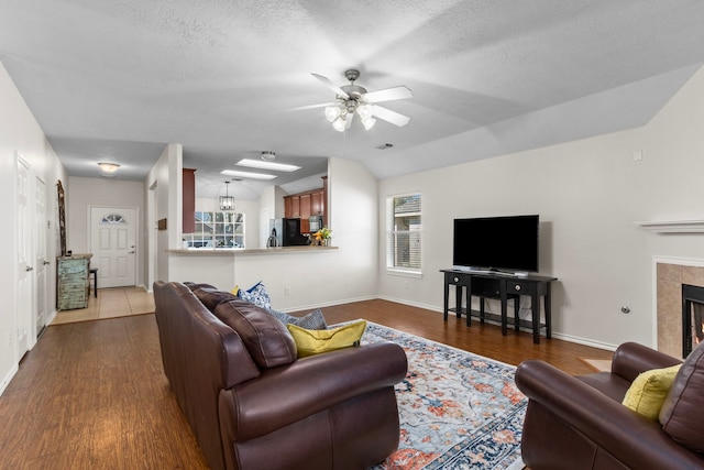 living room featuring lofted ceiling, ceiling fan, a textured ceiling, dark hardwood / wood-style floors, and a tile fireplace