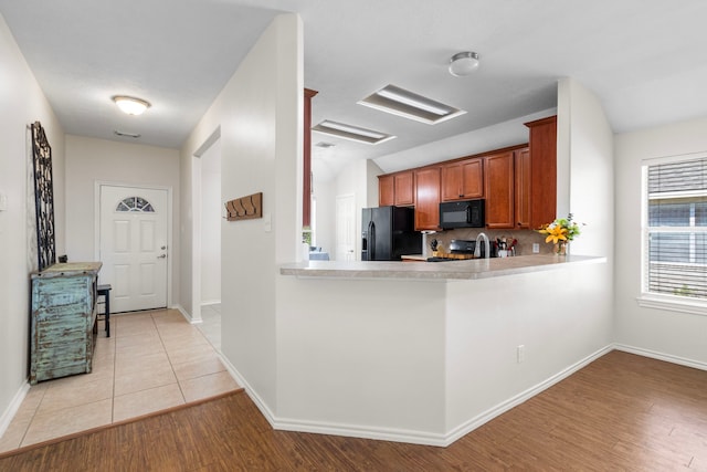 kitchen featuring black appliances, kitchen peninsula, and light wood-type flooring