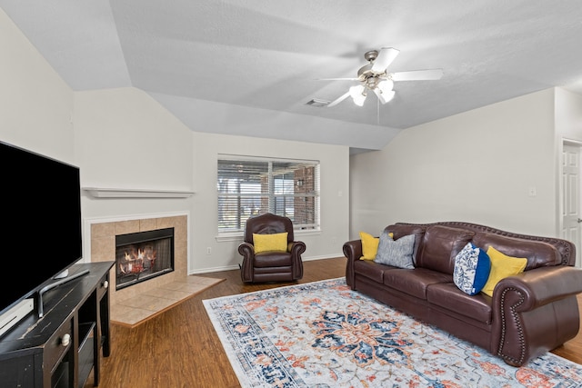 living room with vaulted ceiling, wood-type flooring, a tile fireplace, and ceiling fan