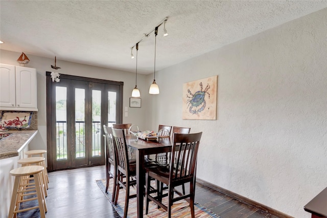 dining area with french doors, rail lighting, dark wood-type flooring, and a textured ceiling