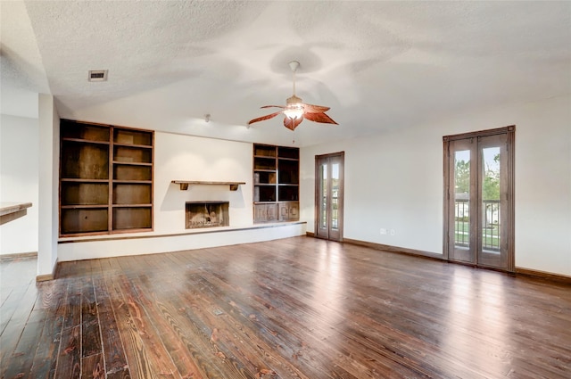 unfurnished living room featuring ceiling fan, built in features, a textured ceiling, and dark wood-type flooring