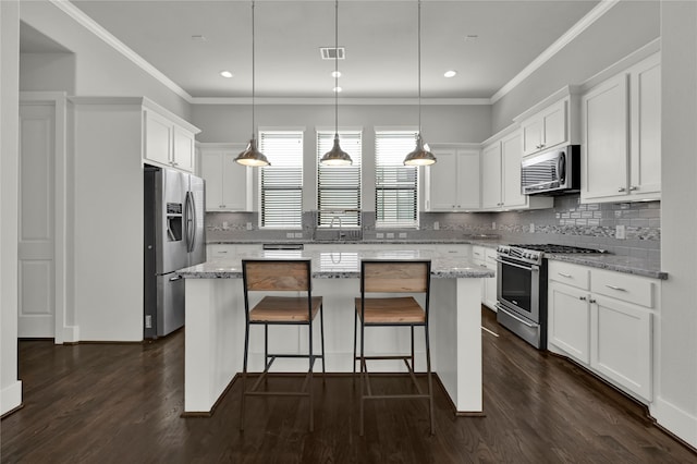 kitchen with appliances with stainless steel finishes, a kitchen island, white cabinets, light stone counters, and dark hardwood / wood-style floors