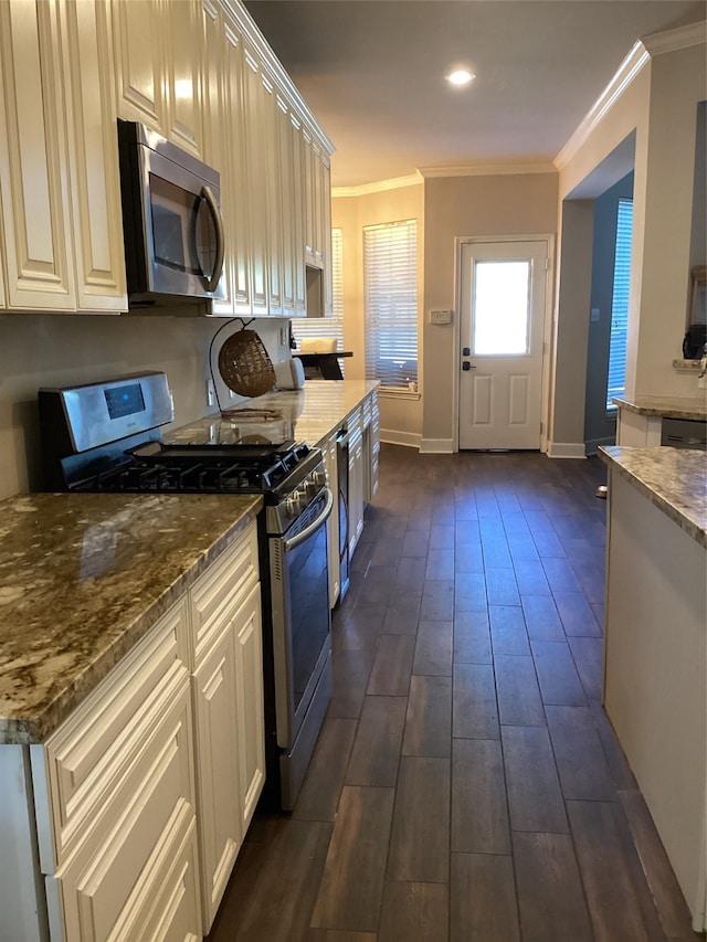 kitchen with appliances with stainless steel finishes, dark hardwood / wood-style floors, dark stone countertops, and ornamental molding