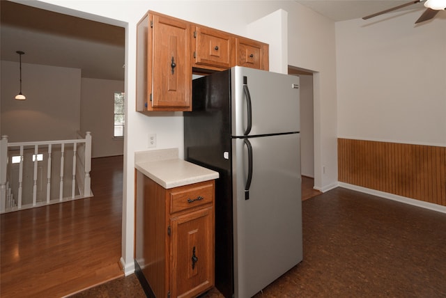 kitchen with dark wood-type flooring, wooden walls, stainless steel fridge, pendant lighting, and ceiling fan