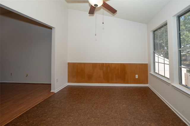 empty room featuring vaulted ceiling, ceiling fan, dark hardwood / wood-style floors, and wood walls