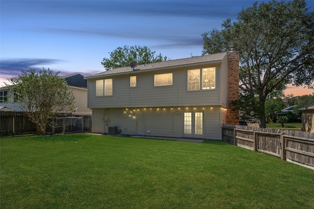 back house at dusk featuring central air condition unit and a lawn