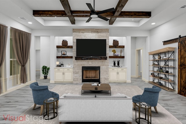 living room featuring a stone fireplace, light hardwood / wood-style flooring, a barn door, and beamed ceiling