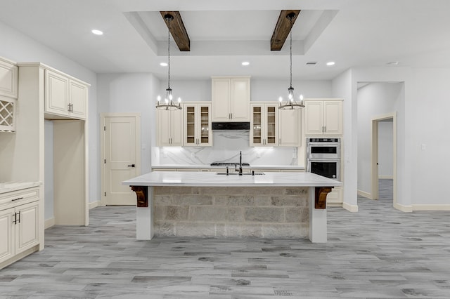 kitchen featuring beam ceiling, an island with sink, light hardwood / wood-style flooring, and pendant lighting