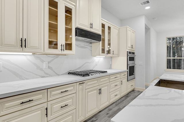 kitchen with cream cabinetry, light stone countertops, stainless steel appliances, and light hardwood / wood-style floors