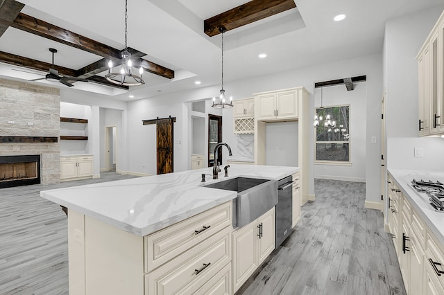 kitchen featuring sink, a barn door, hanging light fixtures, light hardwood / wood-style floors, and a center island with sink