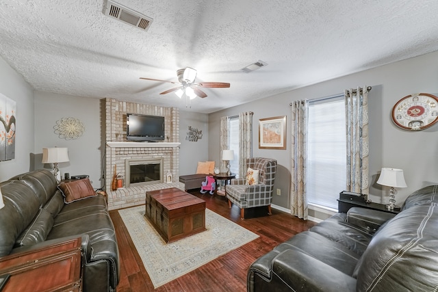 living room with dark wood-type flooring, ceiling fan, a textured ceiling, and a brick fireplace