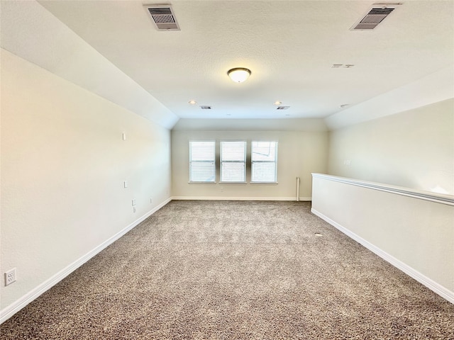 unfurnished room with a textured ceiling, vaulted ceiling, and carpet floors