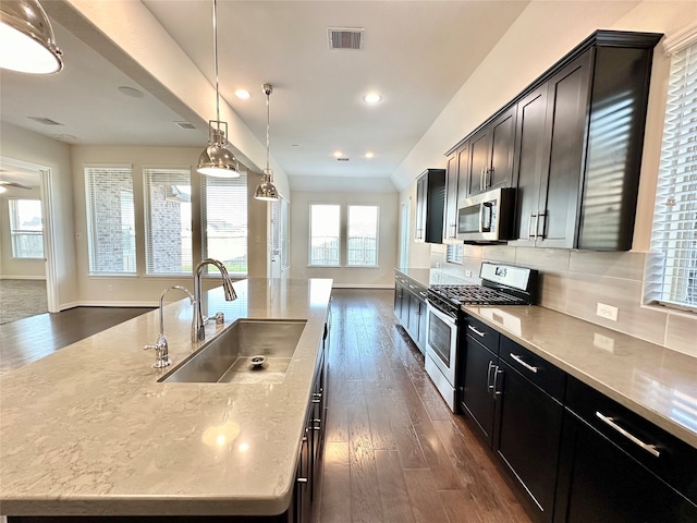 kitchen with dark hardwood / wood-style floors, a center island with sink, sink, decorative light fixtures, and appliances with stainless steel finishes