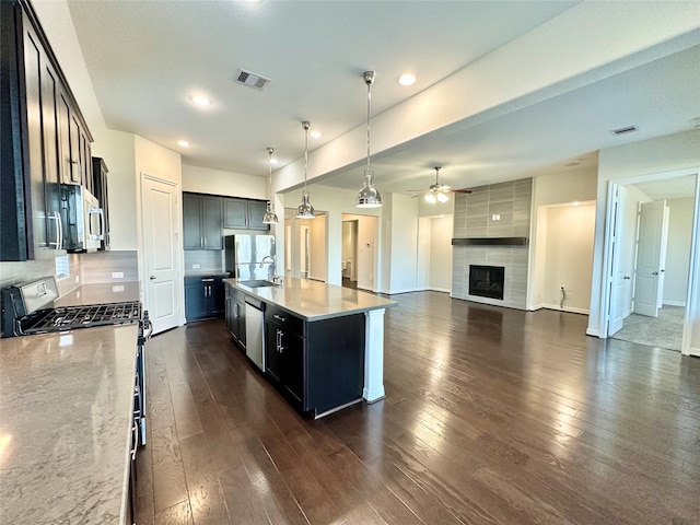 kitchen with a kitchen island with sink, dark hardwood / wood-style floors, hanging light fixtures, stainless steel appliances, and a tile fireplace