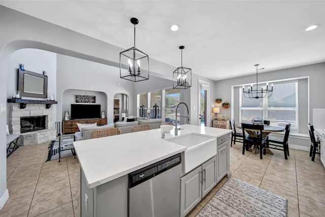 kitchen with dishwasher, sink, hanging light fixtures, a stone fireplace, and an island with sink