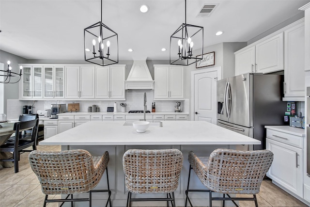 kitchen with stainless steel refrigerator with ice dispenser, a kitchen bar, a center island with sink, white cabinets, and custom exhaust hood