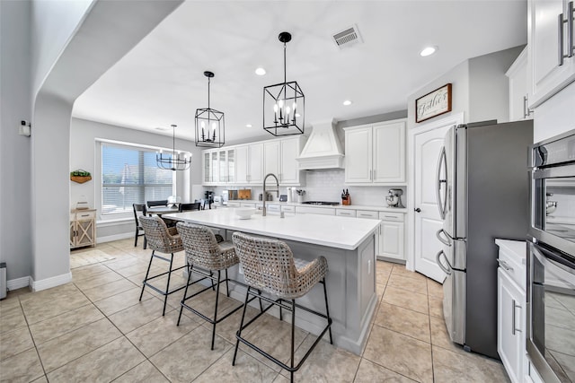 kitchen featuring decorative backsplash, a center island with sink, white cabinets, and custom exhaust hood