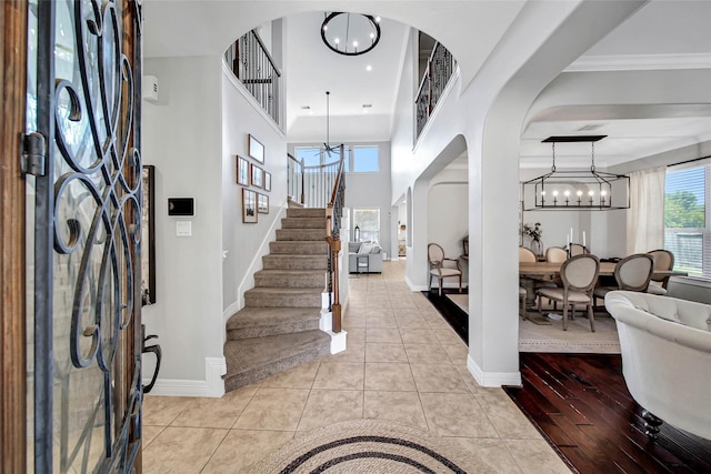 tiled foyer entrance with a towering ceiling, an inviting chandelier, and crown molding