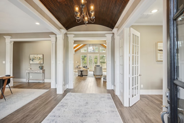 entryway featuring vaulted ceiling, an inviting chandelier, decorative columns, ornamental molding, and light wood-type flooring