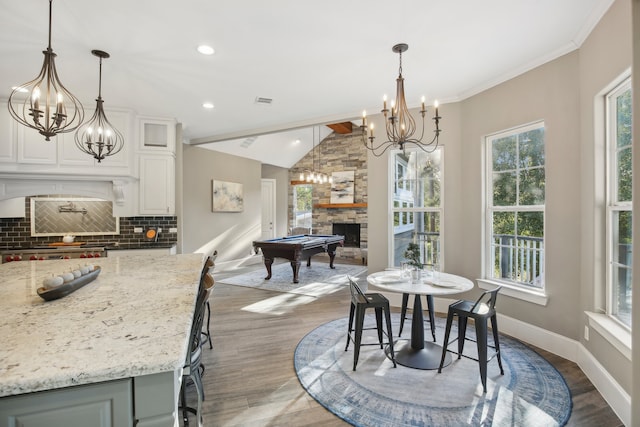 dining room with wood-type flooring, ornamental molding, a fireplace, vaulted ceiling, and pool table