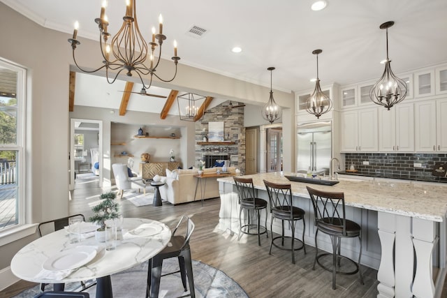 dining space featuring lofted ceiling with beams, a stone fireplace, crown molding, and dark hardwood / wood-style flooring