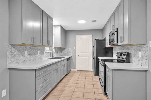 kitchen with gray cabinetry, sink, decorative backsplash, light tile patterned floors, and stainless steel appliances