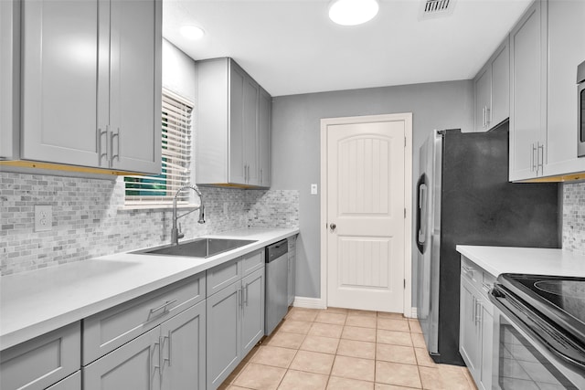 kitchen featuring appliances with stainless steel finishes, backsplash, sink, light tile patterned floors, and gray cabinets