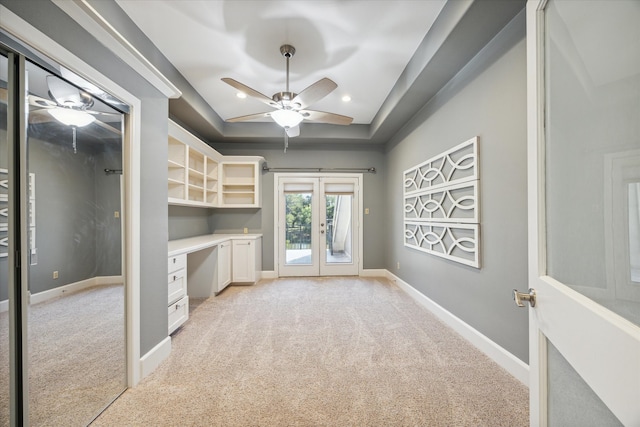 interior space with french doors, built in desk, light colored carpet, a raised ceiling, and ceiling fan