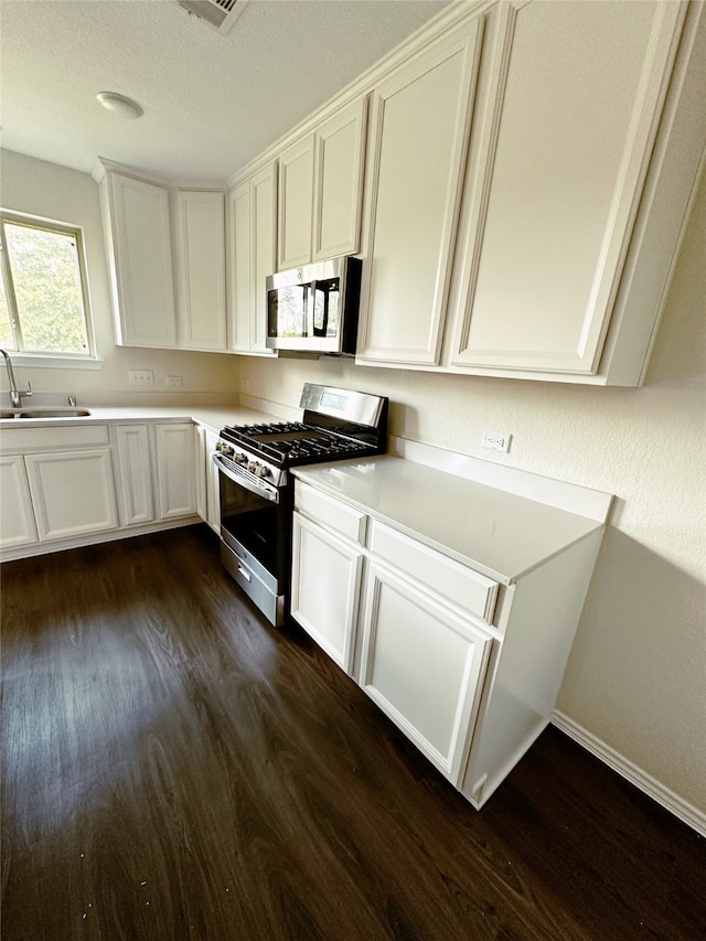 kitchen with appliances with stainless steel finishes, dark hardwood / wood-style floors, sink, and white cabinetry