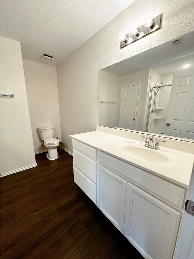 bathroom featuring toilet, wood-type flooring, vanity, a textured ceiling, and walk in shower