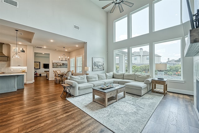 living room with a wealth of natural light, a high ceiling, ceiling fan with notable chandelier, and dark hardwood / wood-style flooring