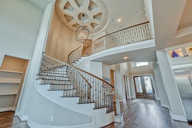 foyer entrance with french doors, a notable chandelier, a towering ceiling, and dark hardwood / wood-style flooring