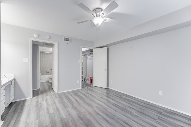 unfurnished bedroom featuring ceiling fan, a spacious closet, connected bathroom, light hardwood / wood-style flooring, and a closet