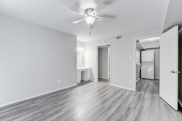 unfurnished bedroom with a spacious closet, ensuite bath, ceiling fan, stacked washing maching and dryer, and light hardwood / wood-style flooring