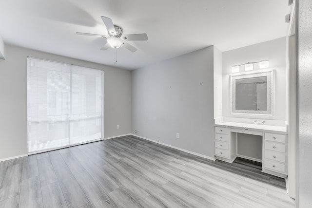 unfurnished bedroom featuring built in desk, ceiling fan, and light hardwood / wood-style flooring