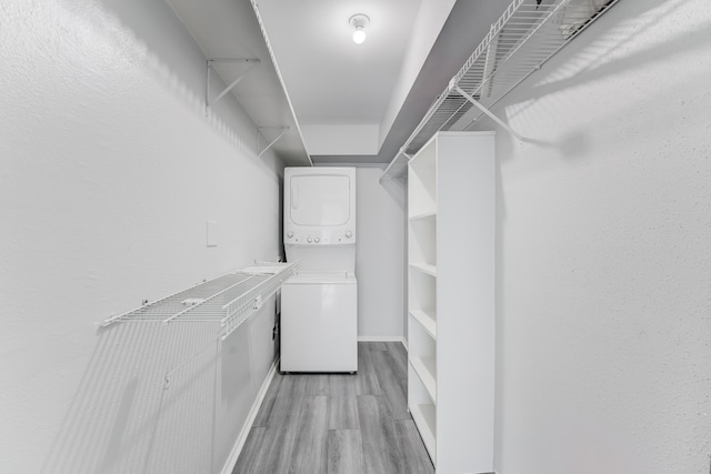 spacious closet featuring stacked washer and dryer and light hardwood / wood-style flooring