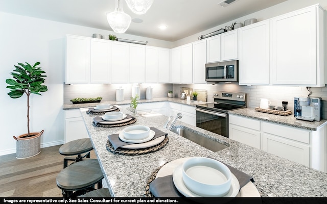 kitchen featuring hardwood / wood-style floors, hanging light fixtures, white cabinetry, sink, and stainless steel appliances