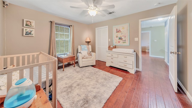 bedroom with ceiling fan, a closet, wood-type flooring, and a nursery area